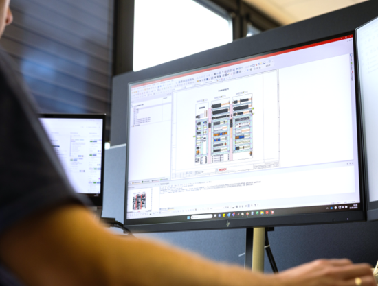 Bosch-Mitarbeiter sitzt vor einem Bildschirm mit einer Montagezeichnung einer Schaltschrank-Grundplatte